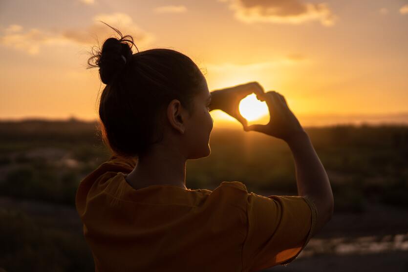 chica viendo un atardecer con buena autoestima y haciendo un corazón con sus manos